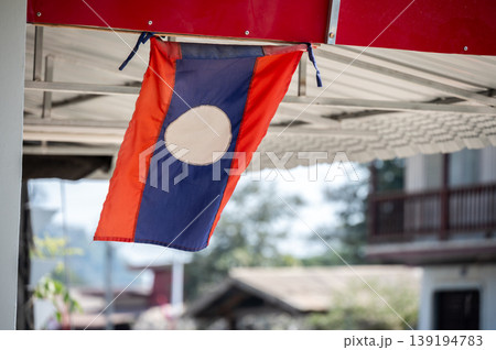 A national flag of Laos hanging infront of local house in Huayxai, Laos. The national flag of Laos was adopted when the country became a people's republic in 1975. A national flag of Laos hanging infront of local house in Huayxai, Laos. The national flag of Laos was adopted when the country became a people's republic in 1975. 139194783