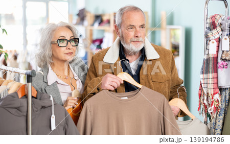 Mature married couple chooses fashionable t-shirt in clothing store Mature married couple chooses fashionable t-shirt in clothing store 139194786