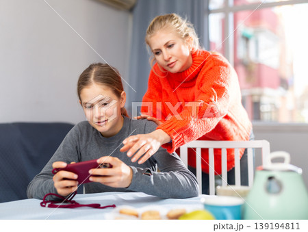 Daughter plays on smartphone while mother tries to talk to her Daughter plays on smartphone while mother tries to talk to her 139194811