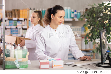 Female pharmacist searches for information about medicines on the Internet, while the assistant places medicines on display 139194862