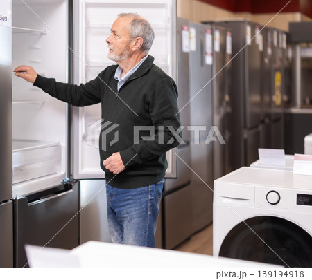 Elderly man choosing a large refrigerator in a store Elderly man choosing a large refrigerator in a store 139194918