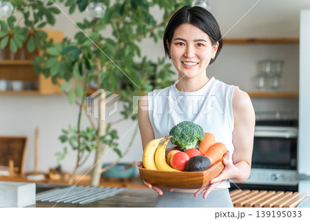 キッチンの前で野菜を持つスポーツウェア姿の若いアジア人女性（野菜不足・栄養バランス・緑黄色野菜） 139195033