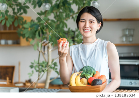 キッチンの前で野菜を持つスポーツウェア姿の若いアジア人女性(野菜不足・栄養バランス・緑黄色野菜) キッチンの前で野菜を持つスポーツウェア姿の若いアジア人女性(野菜不足・栄養バランス・緑黄色野菜) 139195034