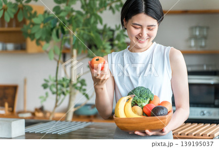 キッチンの前で野菜を持つスポーツウェア姿の若いアジア人女性(野菜不足・栄養バランス・緑黄色野菜) キッチンの前で野菜を持つスポーツウェア姿の若いアジア人女性(野菜不足・栄養バランス・緑黄色野菜) 139195037