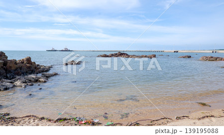 Calm Coastal Water with Distant Industrial Jetty and Rocks 139195088