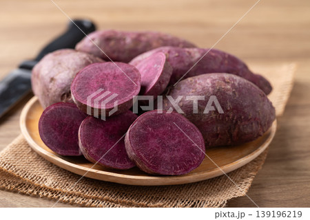 Raw organic purple sweet potatoes on wooden plate Raw organic purple sweet potatoes on wooden plate 139196219