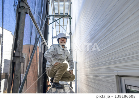 足場の上でしゃがむ住宅外壁工事の作業員 足場の上でしゃがむ住宅外壁工事の作業員 139196608