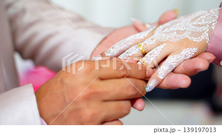 Groom Places Gold Wedding Ring on Bride's Henna-Decorated Hand During Traditional Ceremony 139197013