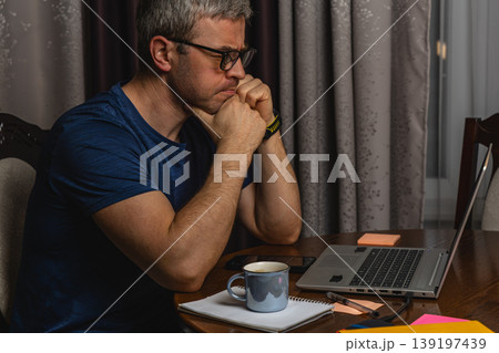 Stressed man working on laptop holding head at night home office Stressed man working on laptop holding head at night home office 139197439