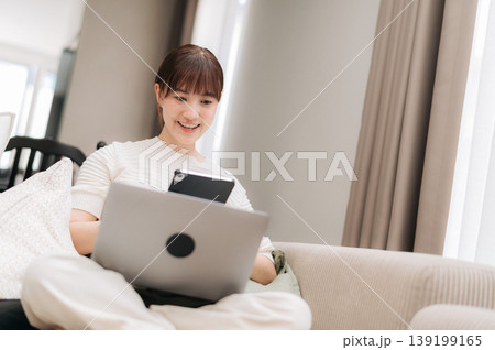 Happy smiling asian woman doing remote business work and study from home looking at laptop computer relaxing on sofa 139199165