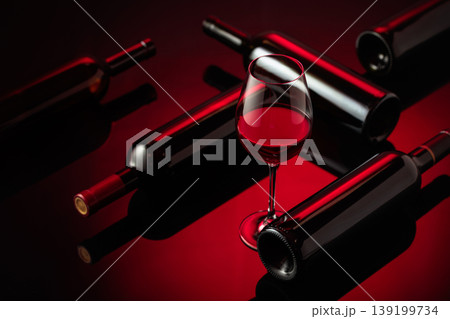 Glass and bottles of red wine on a black reflective background. Glass and bottles of red wine on a black reflective background. 139199734