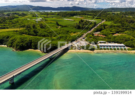 古宇利大橋とエメラルドグリーンの海そして緑に覆われた崖と小さなビーチを真夏に空撮した写真 古宇利大橋とエメラルドグリーンの海そして緑に覆われた崖と小さなビーチを真夏に空撮した写真 139199914