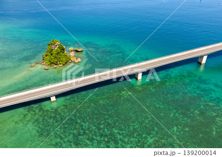 古宇利大橋とエメラルドグリーンの海に浮かぶ小島を真夏の空から捉えた写真 139200014