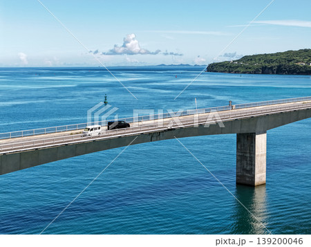 エメラルドブルーの海の上を走る車と古宇利大橋を横位置で切り取った夏の日の写真 139200046