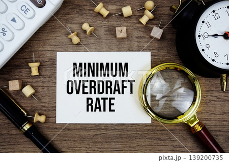 Minimum Overdraft Rate text written on notepad with pen, alarm clock, magnifying glass and calculator on wooden background 139200735