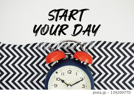 Start Your Day text written on paper rip with alarm clock flat lay on black chevron background 139200770