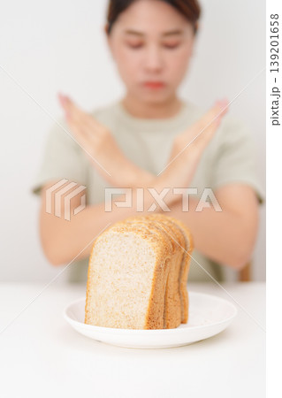 Unhappy woman showing Rejecting gesture and refusing to eat bread. concept of gluten intolerance, gluten sensitivity, carb loading concerns, or a disliking for unhealthy dietary habits 139201658