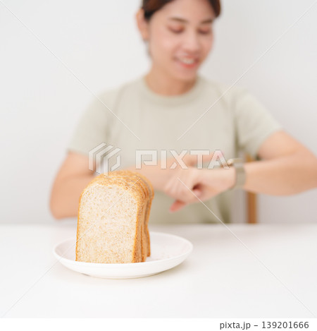 Happy smiling woman with whole wheat bread and time watch. concept of intermittent fasting, IF, meal timing, and choosing healthy carbohydrates for a balanced diet and weight loss management Happy smiling woman with whole wheat bread and time watch. concept of intermittent fasting, IF, meal timing, and choosing healthy carbohydrates for a balanced diet and weight loss management 139201666