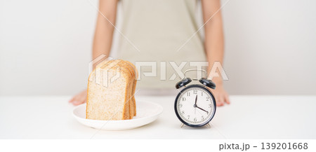 Happy smiling woman with whole wheat bread and alarm clock. concept of intermittent fasting, IF, meal timing, and choosing healthy carbohydrates for a balanced diet and weight loss management Happy smiling woman with whole wheat bread and alarm clock. concept of intermittent fasting, IF, meal timing, and choosing healthy carbohydrates for a balanced diet and weight loss management 139201668