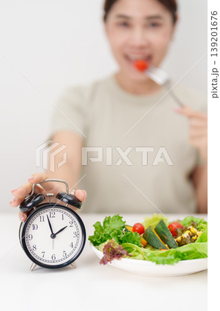 happy smiling woman with fresh organic vegetables plate and alarm clock. intermittent fasting, IF, meal time, nutrition, weight loss, clean eating, Healthy food eating, Wellness, dieting and lifestyle happy smiling woman with fresh organic vegetables plate and alarm clock. intermittent fasting, IF, meal time, nutrition, weight loss, clean eating, Healthy food eating, Wellness, dieting and lifestyle 139201676