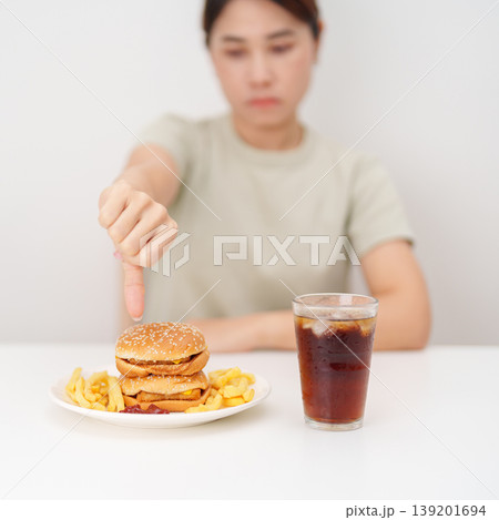 woman showing thumbs down, Rejecting and refusing with Juicy beef burger, potato chips and carbonated Soft drinks. Unhealthy, High calorie, Fast food craving, Obesity, diet, weight loss and junk food woman showing thumbs down, Rejecting and refusing with Juicy beef burger, potato chips and carbonated Soft drinks. Unhealthy, High calorie, Fast food craving, Obesity, diet, weight loss and junk food 139201694