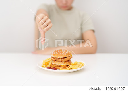 woman showing thumbs down, Rejecting and refusing with Juicy beef burger, potato chips and carbonated Soft drinks. Unhealthy, High calorie, Fast food craving, Obesity, diet, weight loss and junk food 139201697