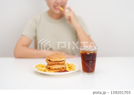 woman eating Juicy beef burger with melted cheddar cheese, potato chips and carbonated Soft drinks. Unhealthy, High calorie, Fast food craving, Obesity, diet, weight loss, junk food and lifestyle 139201703