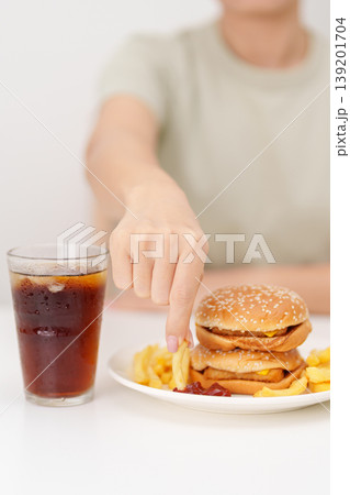 woman eating Juicy beef burger with melted cheddar cheese, potato chips and carbonated Soft drinks. Unhealthy, High calorie, Fast food craving, Obesity, diet, weight loss, junk food and lifestyle woman eating Juicy beef burger with melted cheddar cheese, potato chips and carbonated Soft drinks. Unhealthy, High calorie, Fast food craving, Obesity, diet, weight loss, junk food and lifestyle 139201704