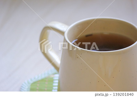 Close up of a warm ceramic mug filled with tea on a green bamboo coaster on a light wooden surface Close up of a warm ceramic mug filled with tea on a green bamboo coaster on a light wooden surface 139201840