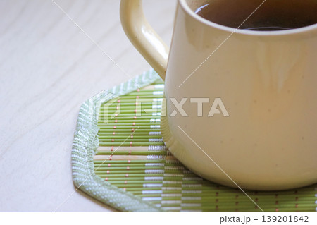 Close up of a warm ceramic mug filled with tea on a green bamboo coaster on a light wooden surface Close up of a warm ceramic mug filled with tea on a green bamboo coaster on a light wooden surface 139201842