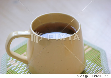 Close up of a warm ceramic mug filled with tea on a green bamboo coaster on a light wooden surface 139201843