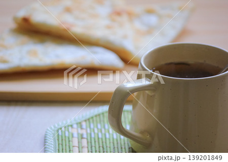 Cozy morning snack featuring warm tea in a ceramic mug and freshly baked flaky flatbread on a wooden board. Cozy morning snack featuring warm tea in a ceramic mug and freshly baked flaky flatbread on a wooden board. 139201849