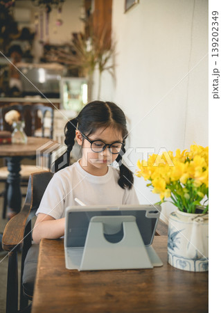 Young girl with glasses enjoying refreshing lemon drink in cozy cafe with beautiful yellow flowers on wooden table, perfect for lifestyle and family themes Young girl with glasses enjoying refreshing lemon drink in cozy cafe with beautiful yellow flowers on wooden table, perfect for lifestyle and family themes 139202349