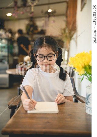 Young girl with glasses enjoying refreshing lemon drink in cozy cafe with beautiful yellow flowers on wooden table, perfect for lifestyle and family themes Young girl with glasses enjoying refreshing lemon drink in cozy cafe with beautiful yellow flowers on wooden table, perfect for lifestyle and family themes 139202350