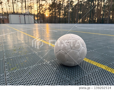 An old soccer ball lies on the artificial surface of a sports stadium in an open wooded area 139202514