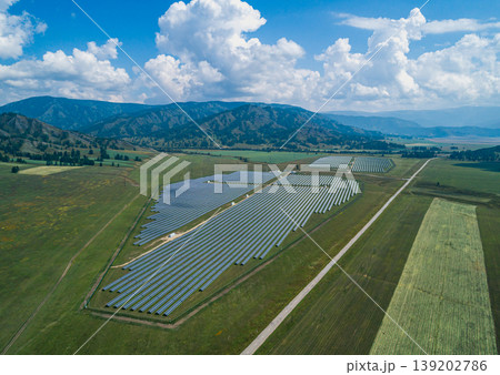 Aerial view captures an extensive solar farm installation spans a verdant valley floor near majestic mountains capturing sun energy Aerial view captures an extensive solar farm installation spans a verdant valley floor near majestic mountains capturing sun energy 139202786