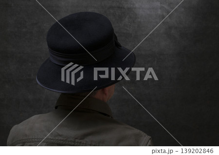 A man in a hat stands with his back against a dark background A man in a hat stands with his back against a dark background 139202846