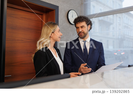 Business Colleagues Discussing Papers at Reception Counter in Elegant Corporate Interior Business Colleagues Discussing Papers at Reception Counter in Elegant Corporate Interior 139202865