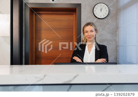 Confident female receptionist standing at modern hotel front desk portrait 139202879