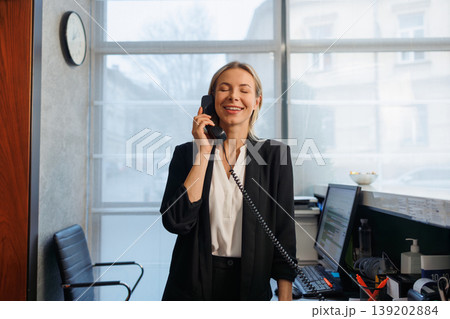 Happy female receptionist answering phone call at hotel reception counter Happy female receptionist answering phone call at hotel reception counter 139202884