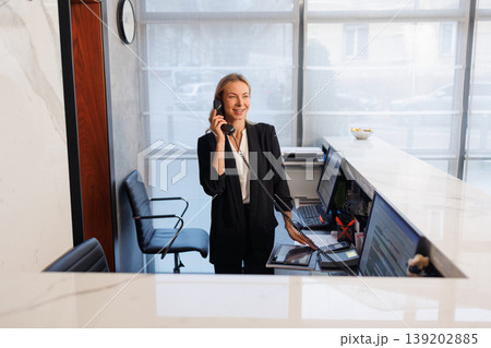Elegant receptionist speaking on phone at modern hotel front desk interior Elegant receptionist speaking on phone at modern hotel front desk interior 139202885