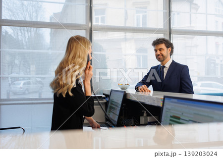 Friendly Receptionist on Phone Assisting Guest at Stylish Hotel Front Desk Interior Friendly Receptionist on Phone Assisting Guest at Stylish Hotel Front Desk Interior 139203024