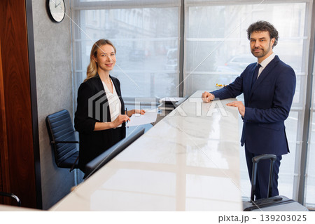 Receptionist and Business Traveler Looking at Camera in Modern Hotel Lobby During Check In Receptionist and Business Traveler Looking at Camera in Modern Hotel Lobby During Check In 139203025