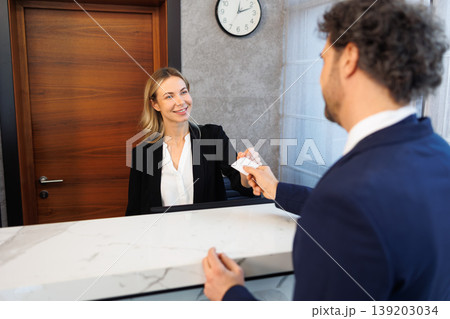 Friendly Female Receptionist Giving Room Key Card to Male Guest at Luxury Hotel Counter Friendly Female Receptionist Giving Room Key Card to Male Guest at Luxury Hotel Counter 139203034
