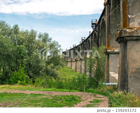 Tall weathered concrete viaduct arches majestically over a vibrant green field on a clear day Tall weathered concrete viaduct arches majestically over a vibrant green field on a clear day 139203172