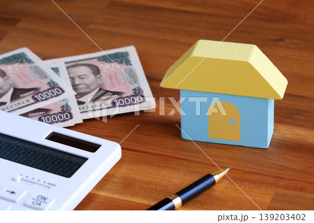 家と一万円札、電卓で、あこがれのマイホームを購入するために資金計画を立てているイメージ 139203402