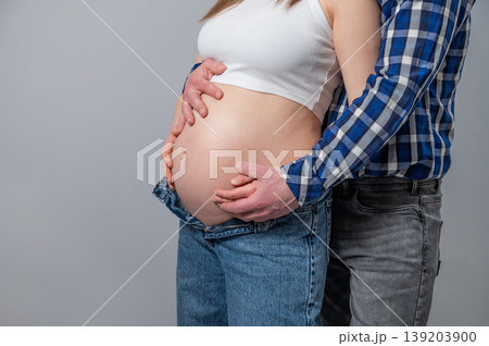 A close-up of a pregnant woman's belly, with her partner's supportive hands on a gray background A close-up of a pregnant woman's belly, with her partner's supportive hands on a gray background 139203900