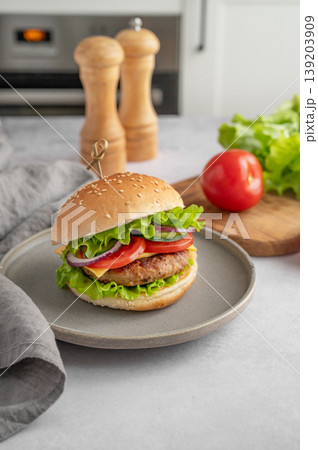 Beef burger with tomato, cheese, and lettuce on a plate on a kitchen table with spice, vegetable Beef burger with tomato, cheese, and lettuce on a plate on a kitchen table with spice, vegetable 139203909