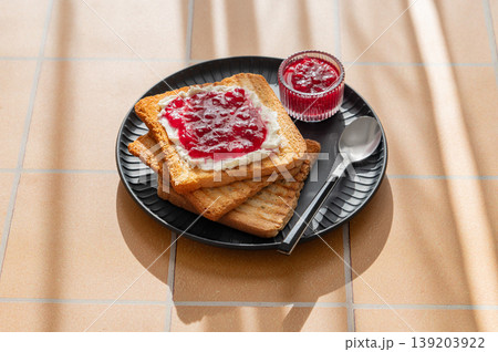 Toast with sweet berry-fruit jam and cream cheese on a dark plate on a yellow tile background Toast with sweet berry-fruit jam and cream cheese on a dark plate on a yellow tile background 139203922