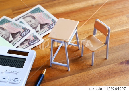高騰する教育費 - 学校の机と椅子、電卓がイメージする、高騰を続けて家計を圧迫する教育費のイメージ 139204007